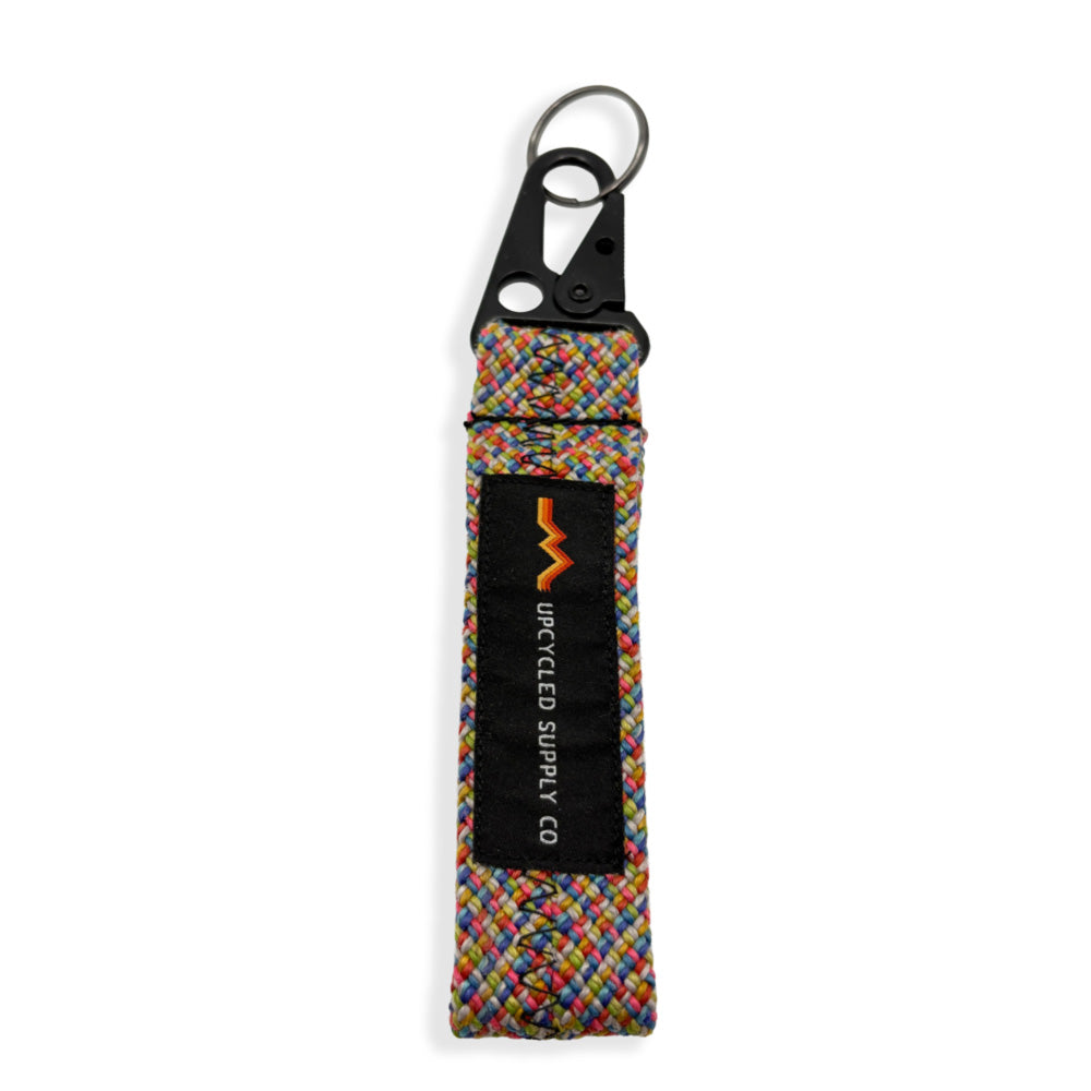 A multicolor braided climbing rope fabric keychain with a black metal carabiner and a black label reading 'UPCYLED SUPPLY CO' on a white background.