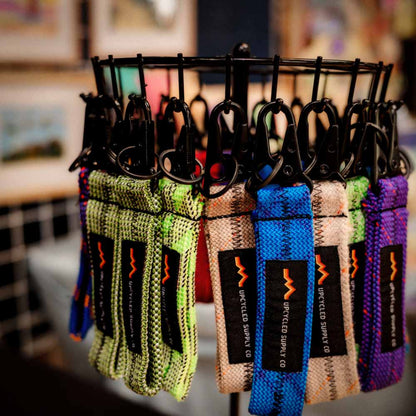 Colorful braided climbing rope fabric keychain with a black metal carabiner and a black label reading 'UPCYLED SUPPLY CO' on a stand.