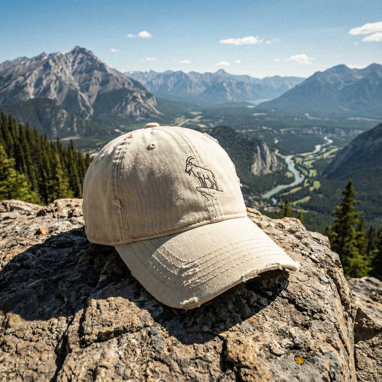 Beige cotton distressed dad cap with embroidered mountain goat on a rock with a mountainous landscape in the background by Kempain Family Outfitters.
