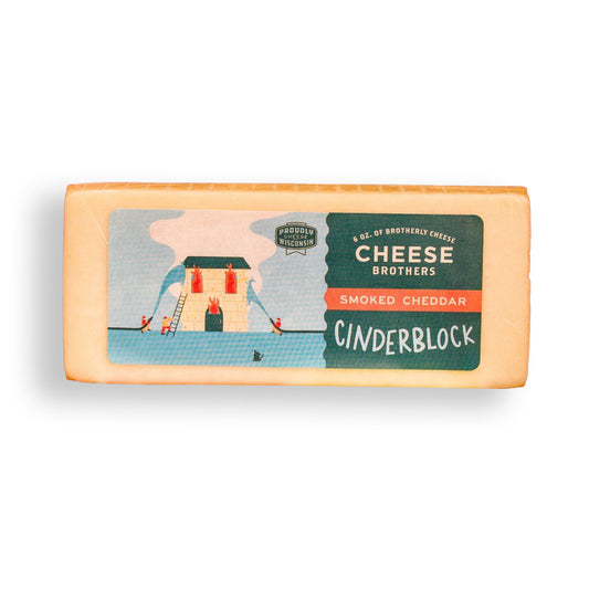 A rectangular package of Cheese Brothers Smoked Cheddar Cinderblock cheese on a clean white background. The package features a colorful illustration of a chimney with smoke and figures, alongside text identifying the product.