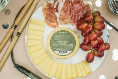 Platter with cheese, prosciutto, and grapes on a table showcasing the back nutrition label for the Cheese Brothers smoked provolone cheese. 