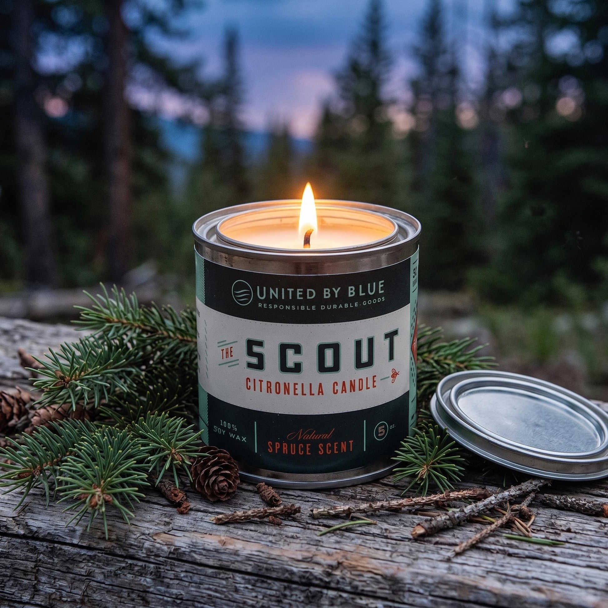 100% GMO-free soy wax for a soot-free, non-toxic burn the 5oz Scout Citronella Candle from United By Blue is displayed lit in the woods.