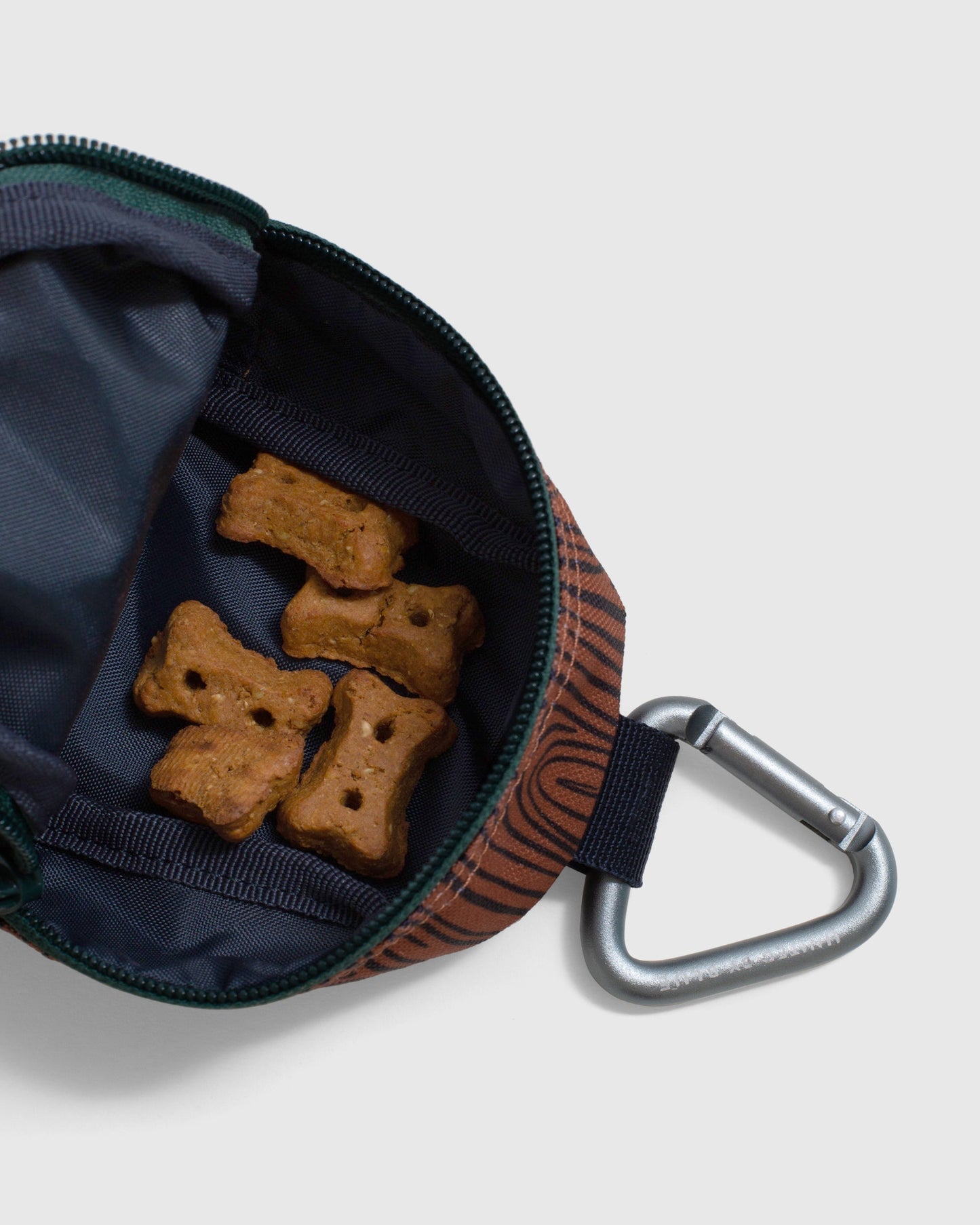 Crafted from 100% (R)evolution™ recycled polyester made from post-consumer plastic bottles The Dog Waste Bag Dispenser in from United By Blue is displayed on a white background with zipper open showing the pouch for dog bones.