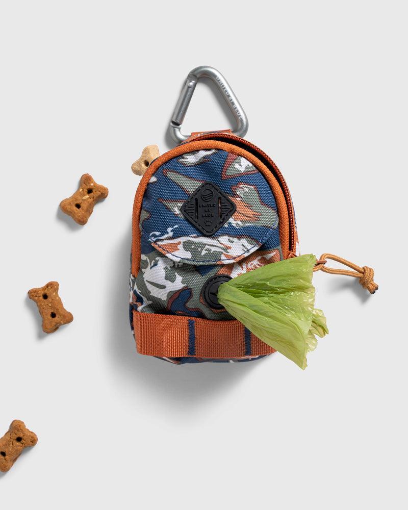 Crafted from 100% (R)evolution™ recycled polyester made from post-consumer plastic bottles The Dog Waste Bag Dispenser in Lakeside Camo from United By Blue is displayed on a white background with dog bones and recycled green bags.