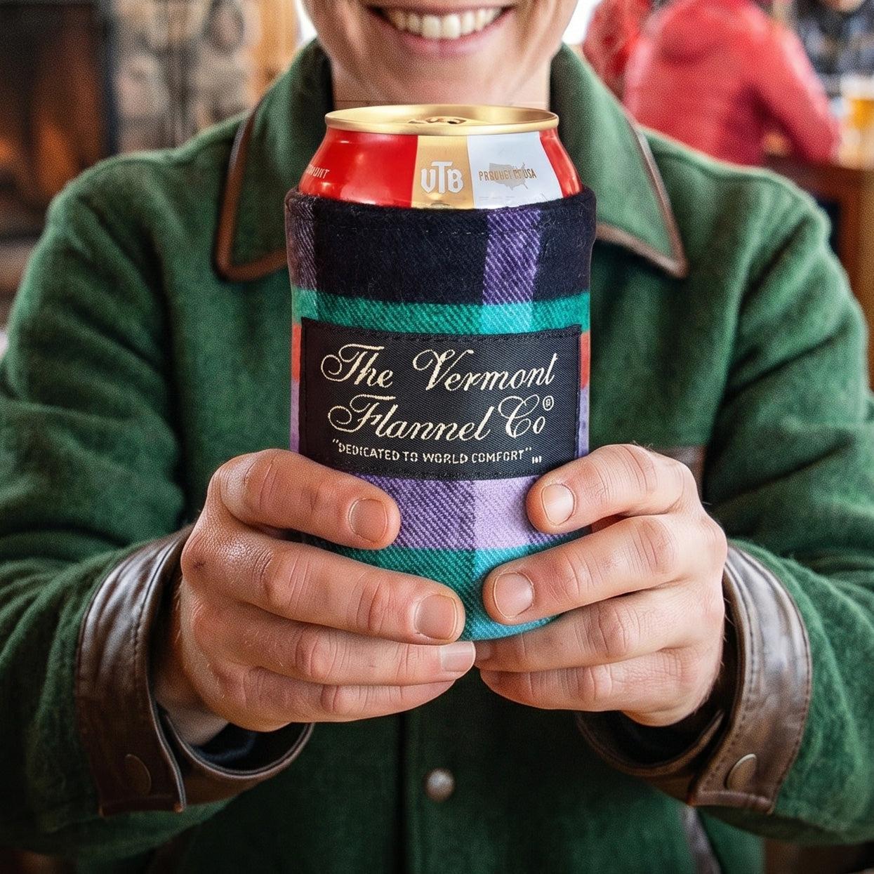 Person holding a can with a colorful flannel sleeve, featuring 'The Vermont Flannel Co.' branding.