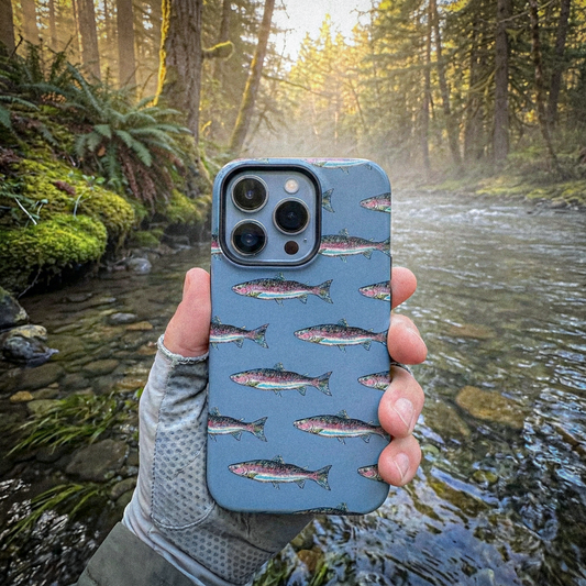 Phone case with fish pattern held in front of a forest stream