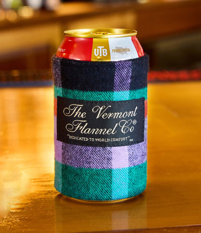Can with a colorful flannel sleeve on a wooden surface, featuring 'The Vermont Flannel Co.' branding.