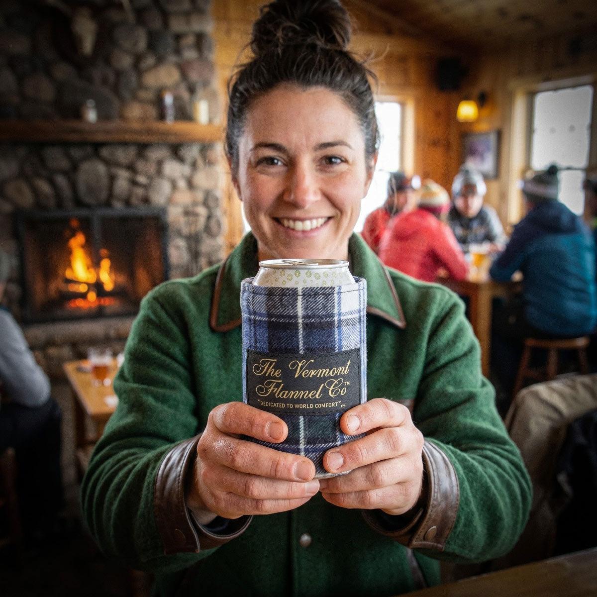 Woman holding a plaid container labeled 'The Vermont Flannel Co.' in a cozy indoor setting.