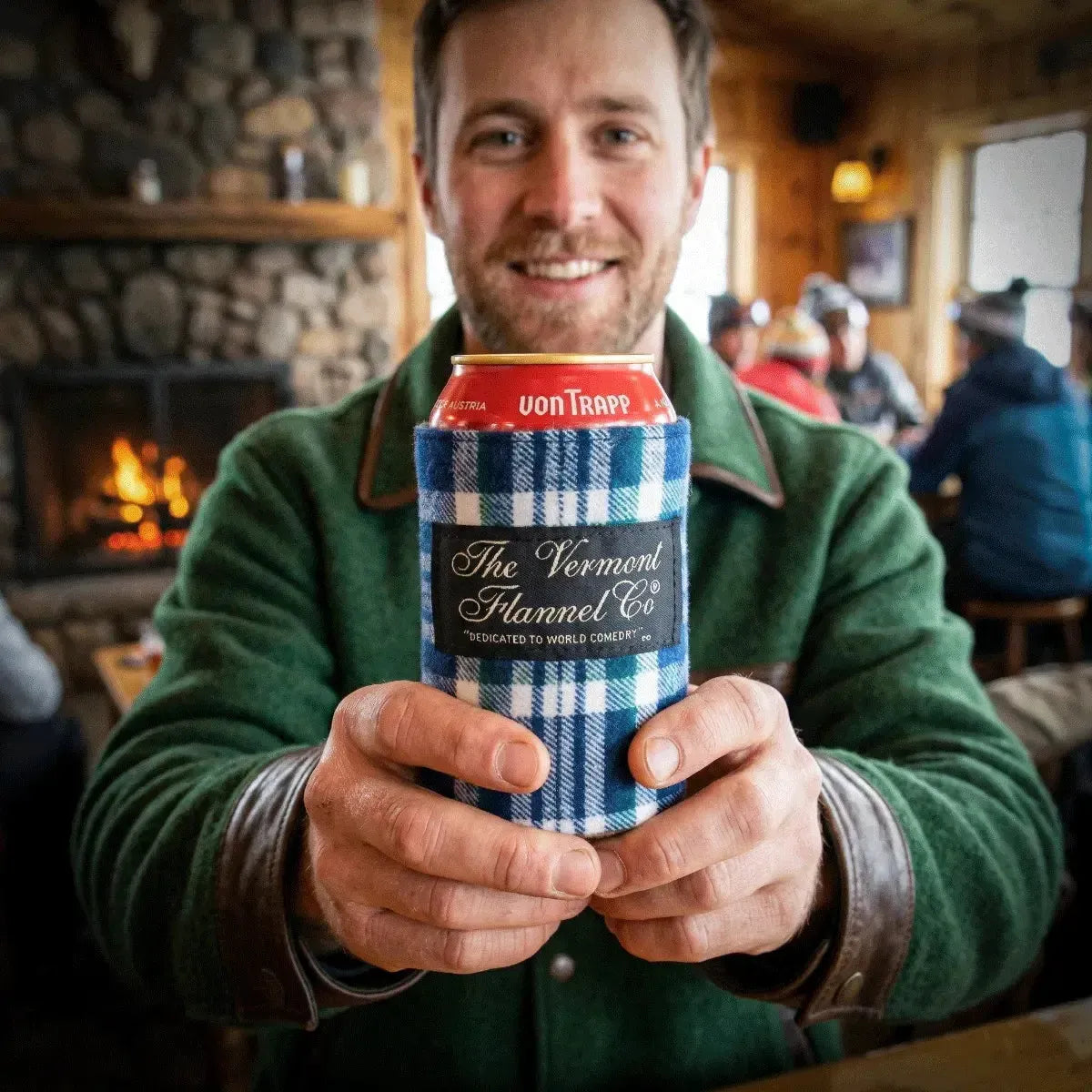 Man holding a can with 'The Vermont Flannel Co.' branding in a cozy indoor setting.