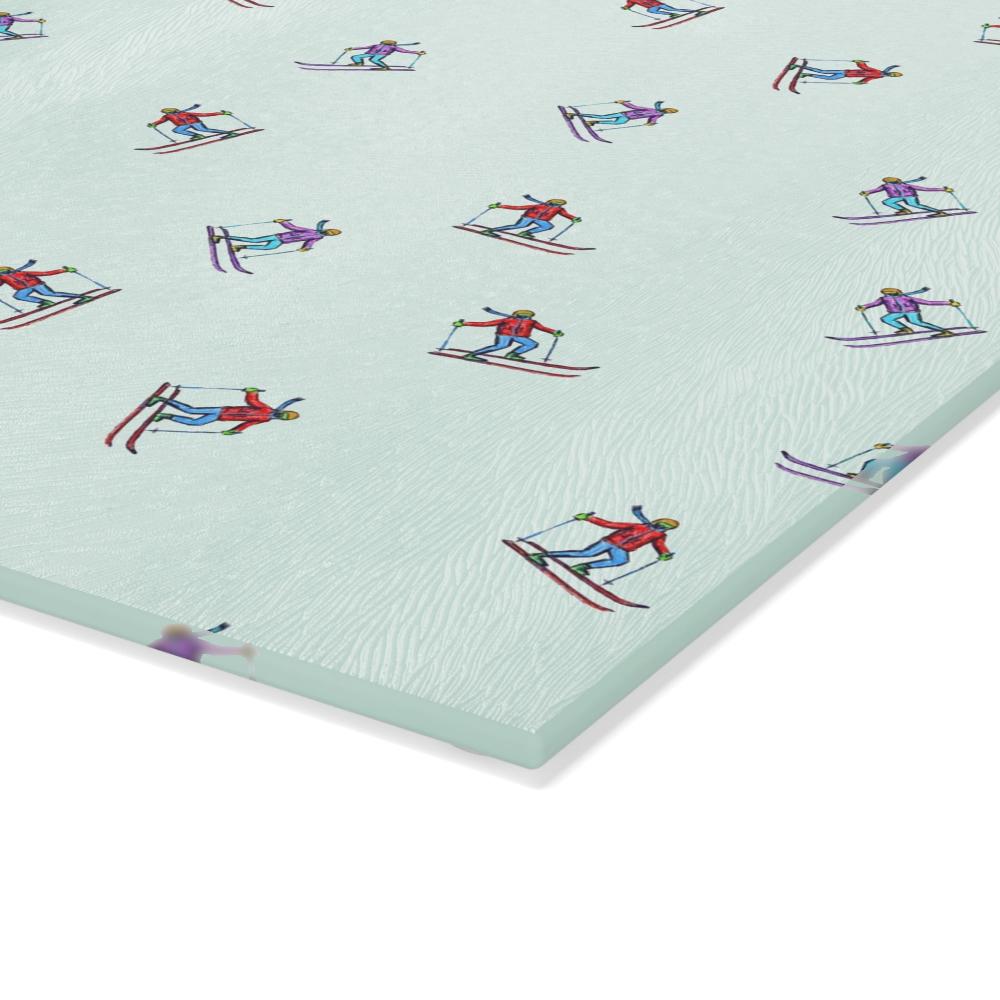 Close-up view of the corner of a glass cutting board featuring an illustrated skier pattern, titled 'Carving the Slopes,' showcasing the design details and quality of the board.