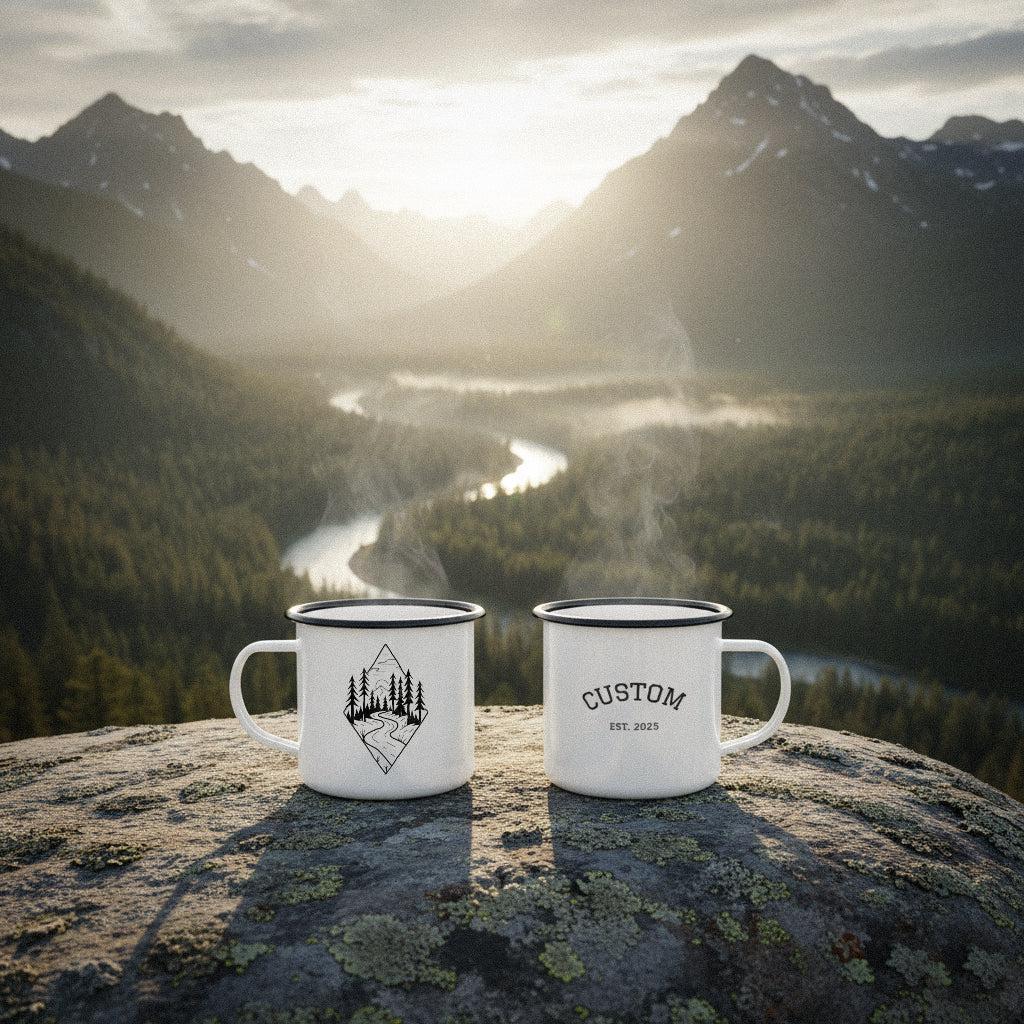 Two personalized mountain peak pursuit mugs resting on a rock overlooking a winding river and pine forest.