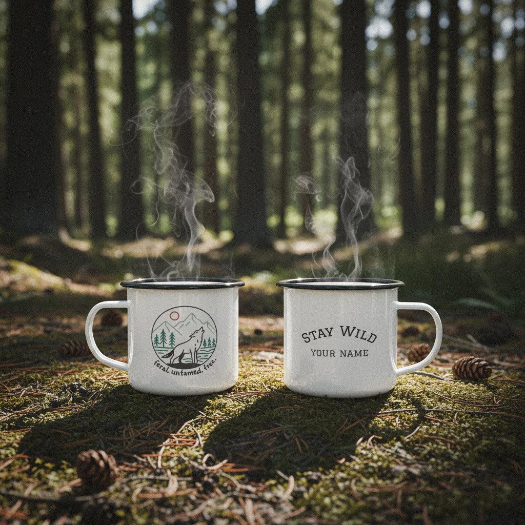 Two personalized wolf howling camp mugs on a mossy forest floor with pinecones and sunlight.