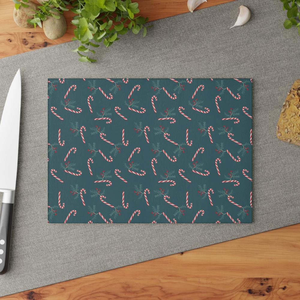 Glass cutting board with a candy cane and holly pattern, displayed on a kitchen table in a lifestyle setting, adding a festive touch to holiday decor.