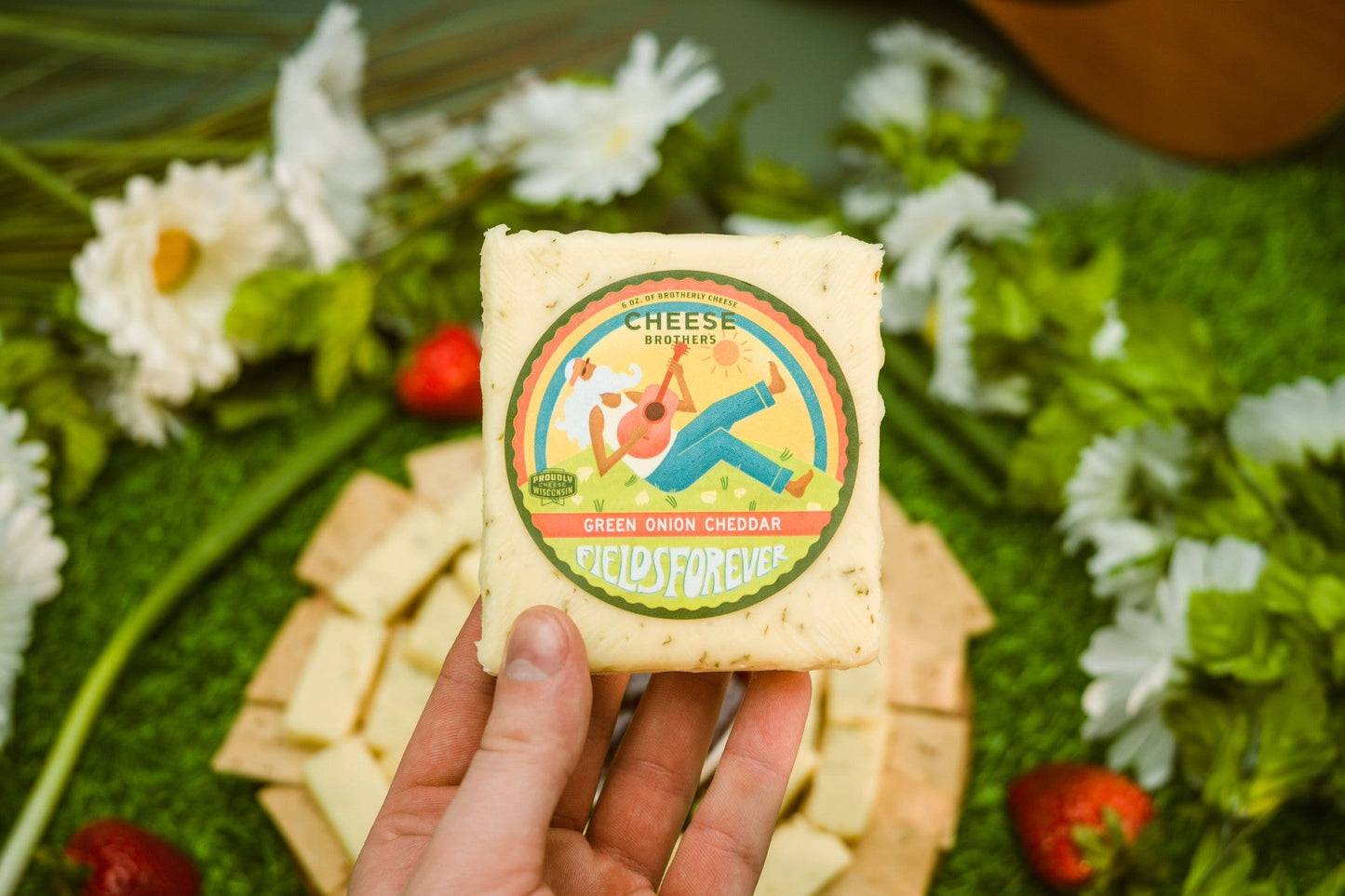 A block of Green Onion Cheddar held above a cheese board by Cheese Brothers, Inc. sold by Kempain Family Outfitters.