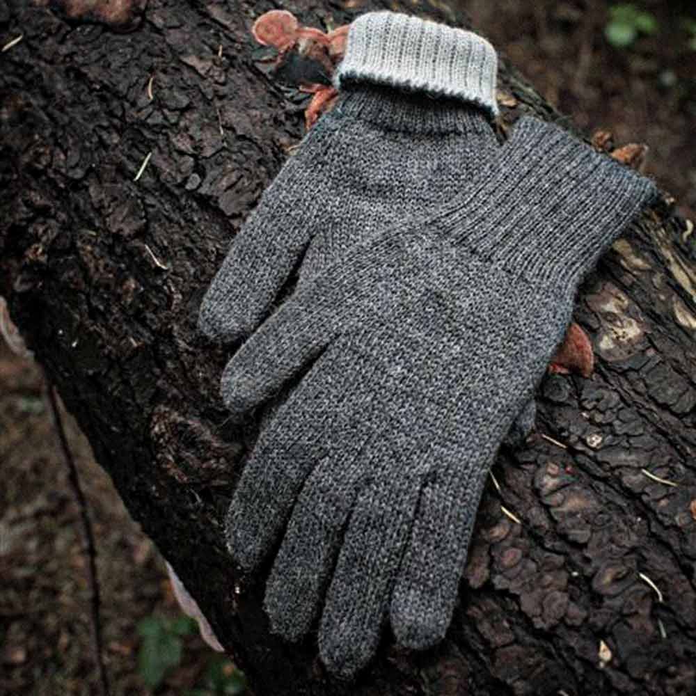 A pair of gray alpaca knit gloves with ribbed cuffs, resting on a dark textured tree trunk outdoors.