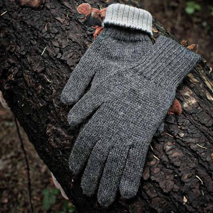 A pair of gray alpaca knit gloves with ribbed cuffs, resting on a dark textured tree trunk outdoors.