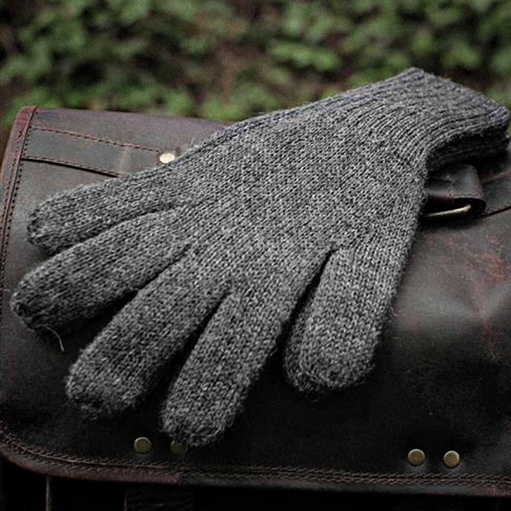 A dark gray alpaca knit glove resting on a brown leather bag, with a blurred green outdoor background.