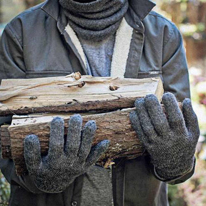 A person outdoors wearing dark gray alpaca gloves, a gray turtleneck, and a dark jacket while holding stacked logs.