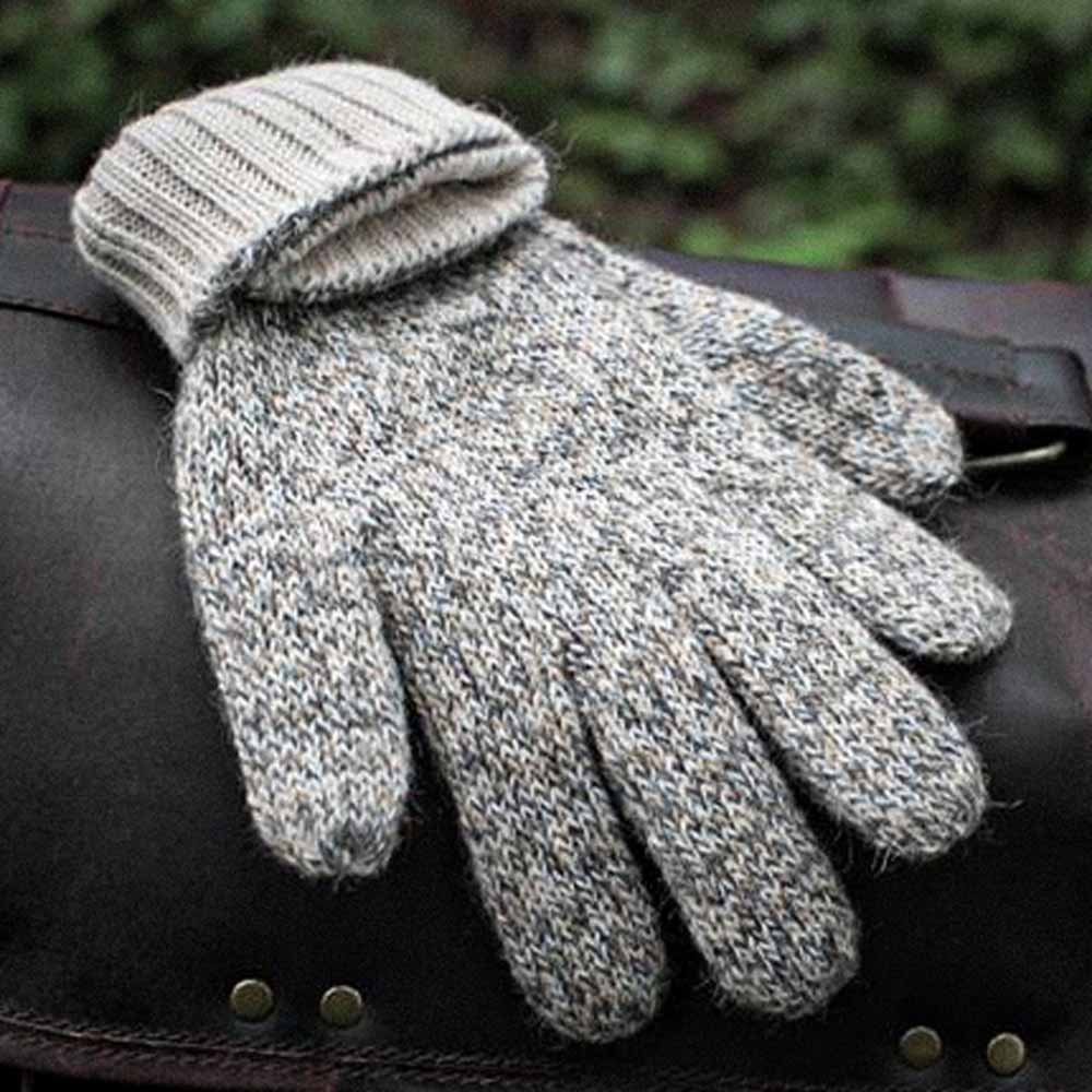 A single alpaca knit glove in a heathered light gray and white blend, laid flat on a dark leather surface with a blurred green outdoor background.