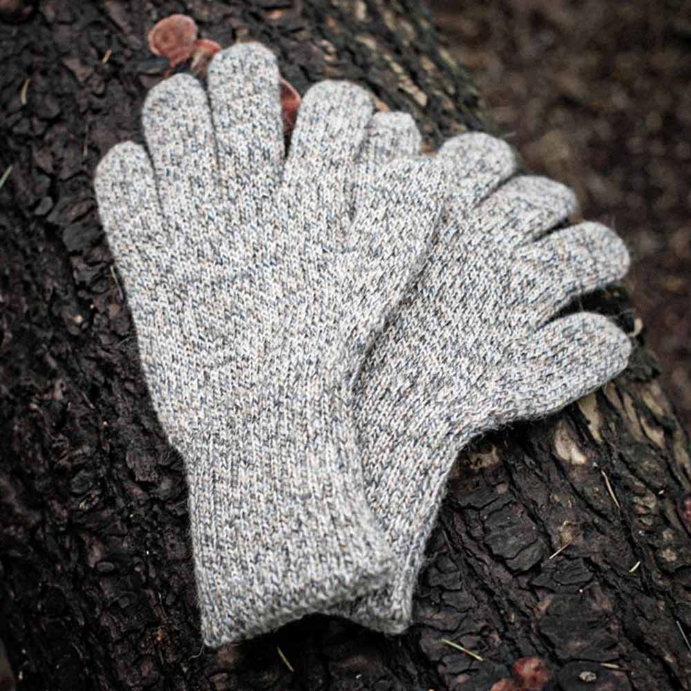 A pair of heather gray alpaca knit gloves resting on a dark textured tree trunk outdoors.