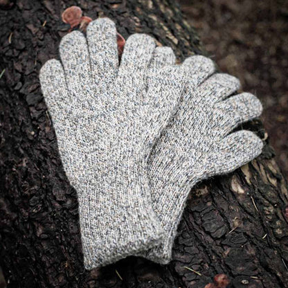 A pair of heather gray alpaca knit gloves resting on a dark textured tree trunk outdoors.