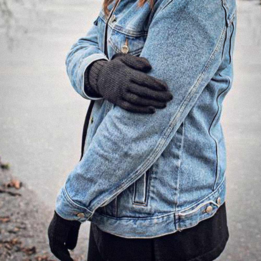 A person wearing a light blue denim jacket and dark brown knit alpaca gloves, standing outdoors with arms crossed.