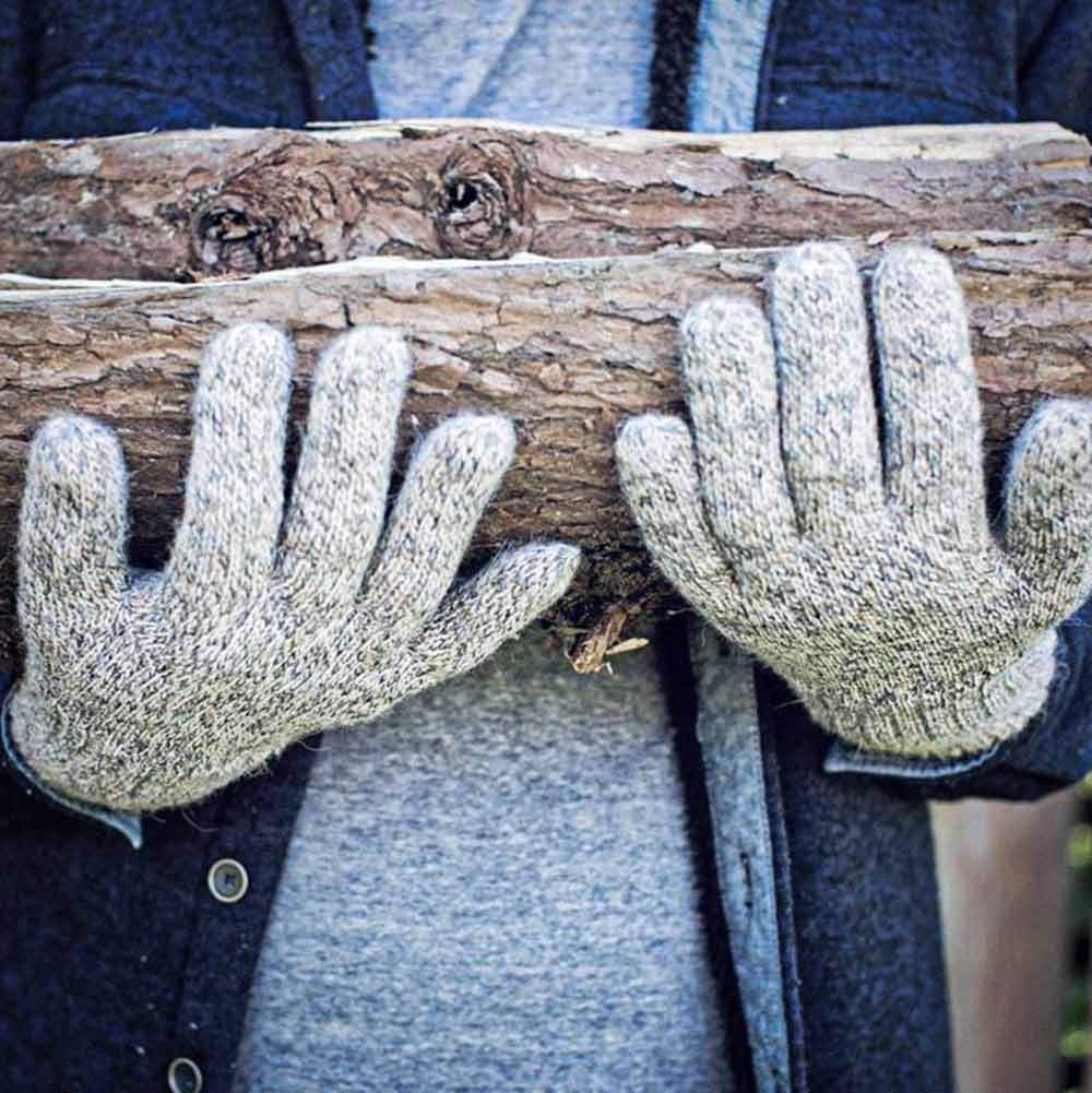 Close-up of a person wearing thick alpaca knit gloves while holding a rough tree branch outdoors.