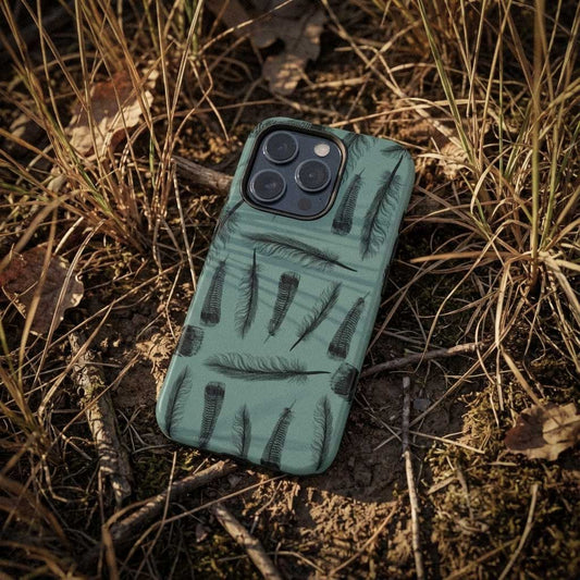 Photograph of phone case with turkey feather pattern on grass. The feathers are detailed pen and ink illustrations with teal base color for iPhone. 