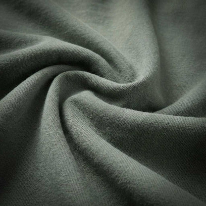 Macro detail of 100% ring-spun US cotton fabric in muted sage green, showing the heavyweight texture and natural fiber weave with zero synthetic blends.