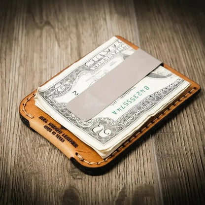Leather money clip holding a dollar bill on a wooden surface