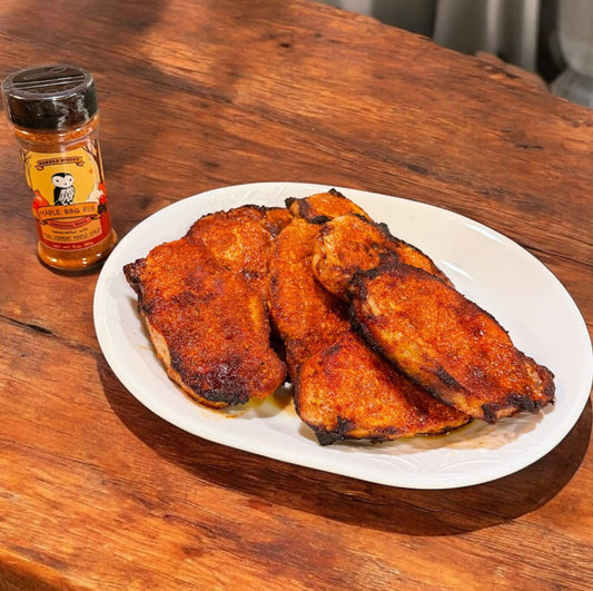 Plated barbecue pork on a wooden table with a bottle of Maple BBQ Rub by Barred Woods Maple Company.