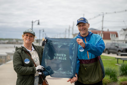 A couple holding up a United By Blue bandana as part of the reusable do it yourself trash cleanup Kit - recycled and organic by United By Blue.