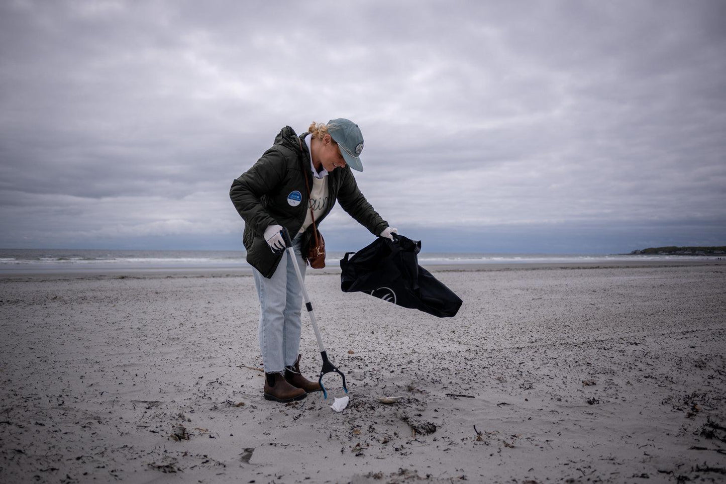A woman at the beach using the reusable do it yourself trash cleanup Kit by United By Blue.