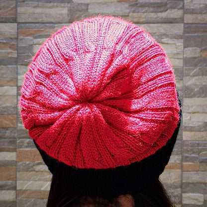 Red knitted beanie worn by a person against a stone wall background