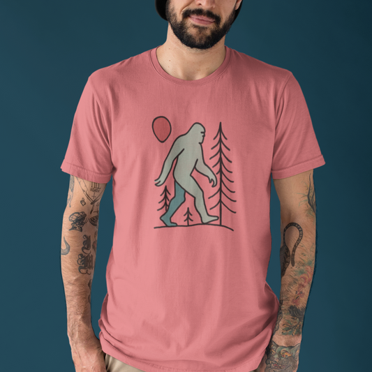 Model wearing the Sasquatch Red Moon Forest Tee with a clean solid background, showing the mystical forest and red moon line art design printed on a coral silk unisex t-shirt.

