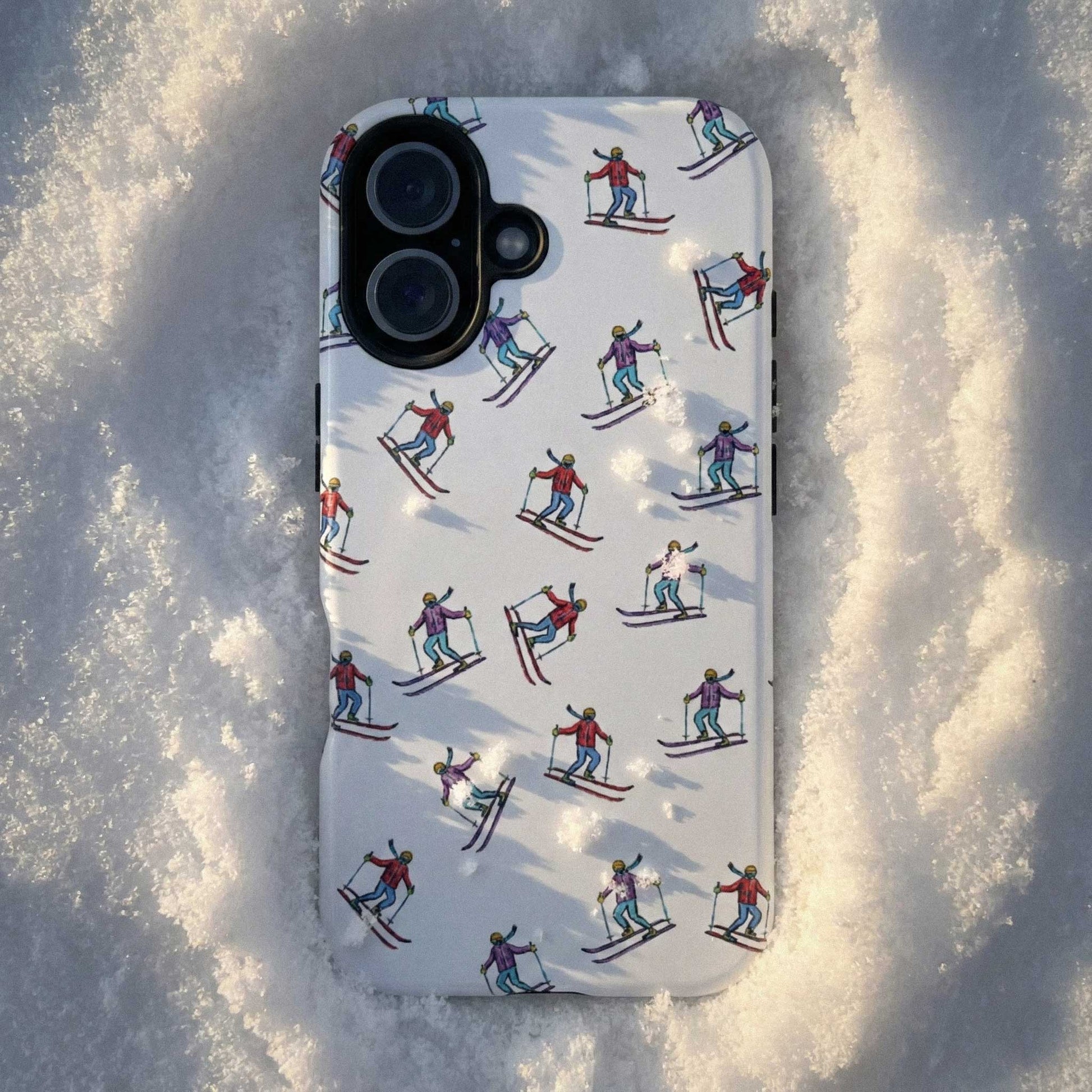 Lifestyle shot of a cell phone case with illustrated skiers resting on snow, highlighting its outdoor-inspired skiing pattern and durable design.
