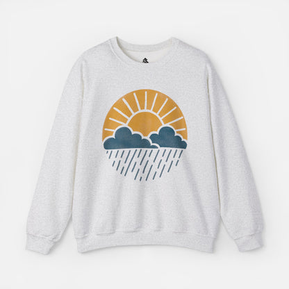 Flat lay of Sun Over Clouds Minimalist Sweatshirt in grey fabric on a white background, featuring a simple line art illustration of a sunrise over clouds and rain within a subtle circle, printed on a classic unisex crewneck.