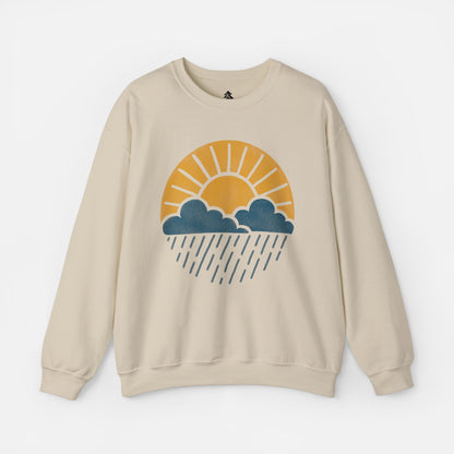 Flat lay of Sun Over Clouds Minimalist Sweatshirt in sand color fabric on a white background, featuring a simple line art illustration of a sunrise over clouds and rain within a subtle circle, printed on a classic unisex crewneck.