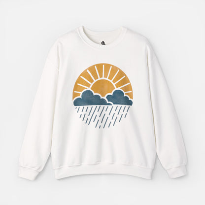 Flat lay of Sun Over Clouds Minimalist Sweatshirt in white fabric on a white background, featuring a simple line art illustration of a sunrise over clouds and rain within a subtle circle, printed on a classic unisex crewneck.