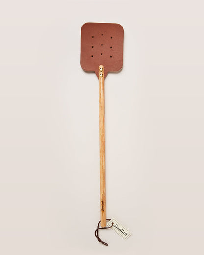 The oak brown Leather Huntsman Flyswatter by Farmhouse Pottery sold by Kempain Family Outfitters displayed on a solid gray background.