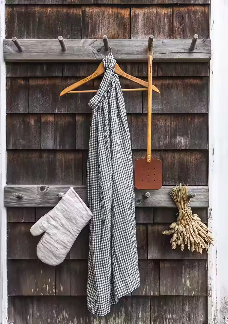 The Leather Huntsman Flyswatter displayed on a wooden hook on rustic cedar siding to showcase the farmhouse appeal.