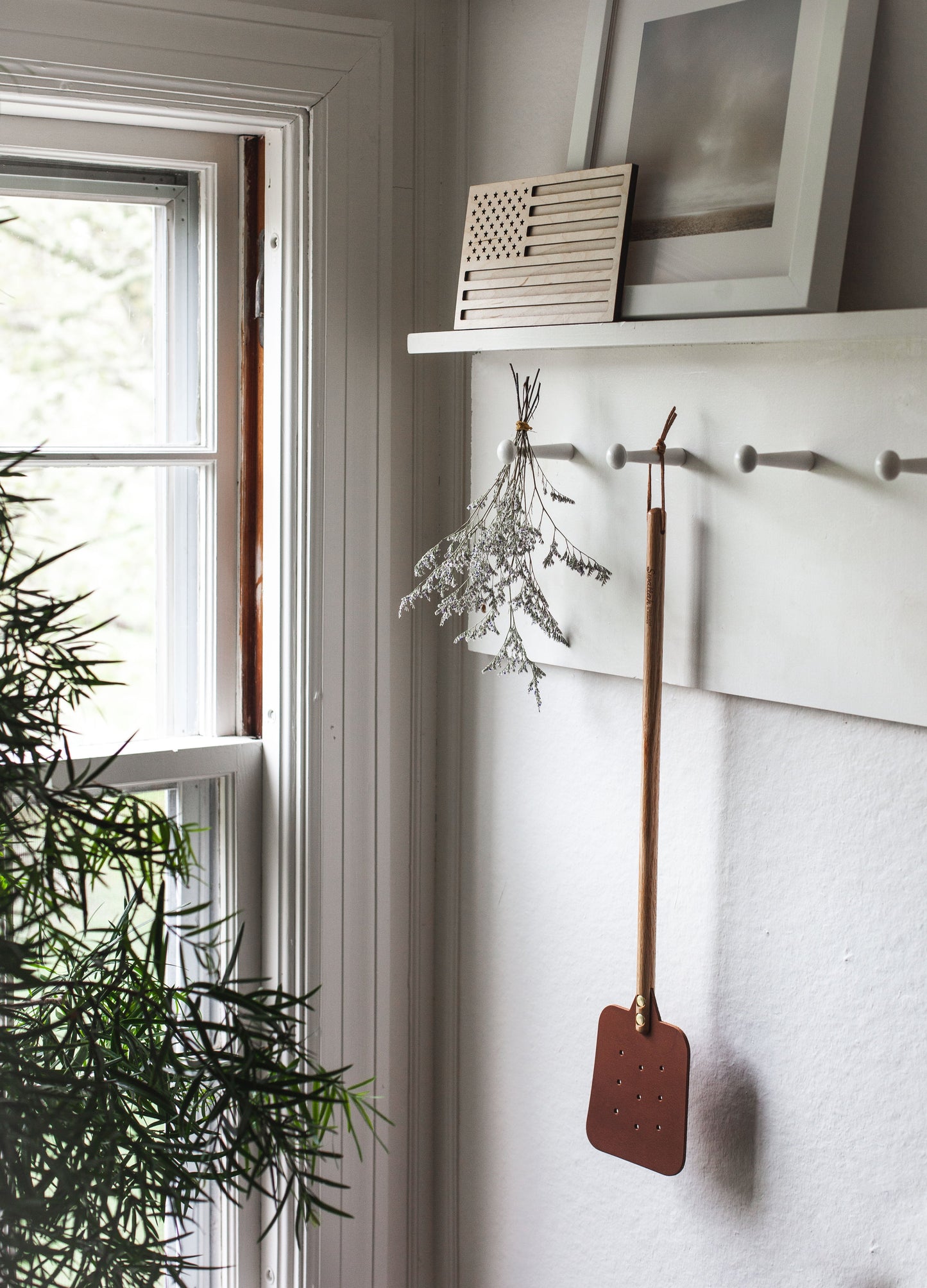 The Leather Huntsman Flyswatter by Farmhouse Pottery sold by Kempain Family Outfitters displayed on a hook in farmhouse setting.