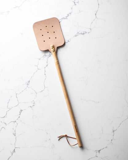 The maple color Leather Huntsman Flyswatter by Farmhouse Pottery on a white marble background sold by Kempain Family Outfitters.