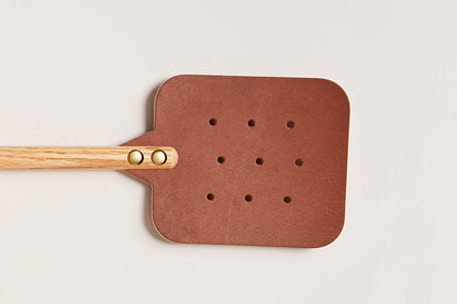 The oak brown Leather Huntsman Flyswatter by Farmhouse Pottery sold by Kempain Family Outfitters displayed on gray background featuring a close view of the leather and brass hardware.