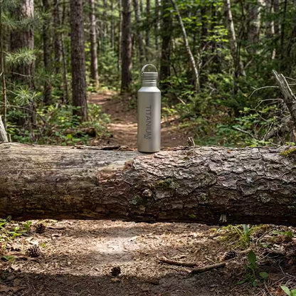 A VARGO titanium water bottle with 'TITANIUM' printed vertically, sitting on a fallen log in a forest setting.