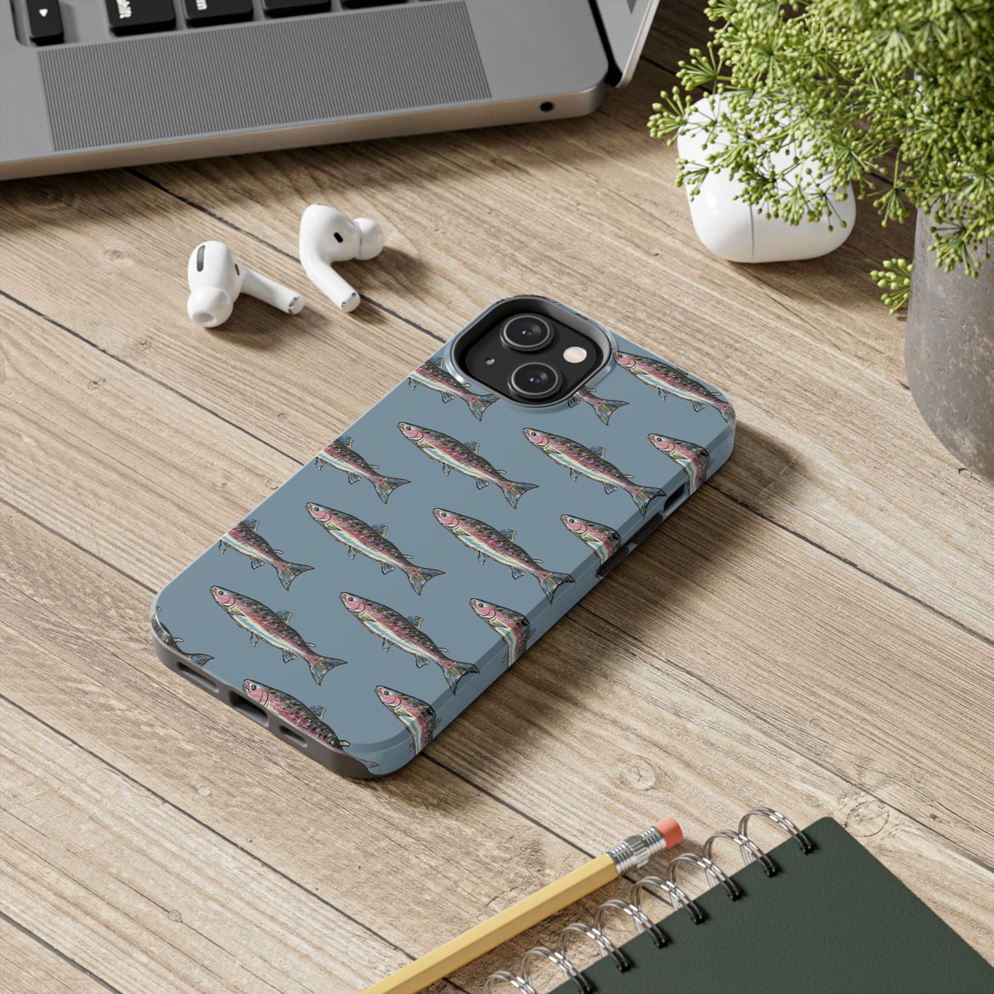 Illustrated rainbow trout durable phone case for anglers on a desk lifestyle view.  Compatible with iPhone and Samsung Models. 