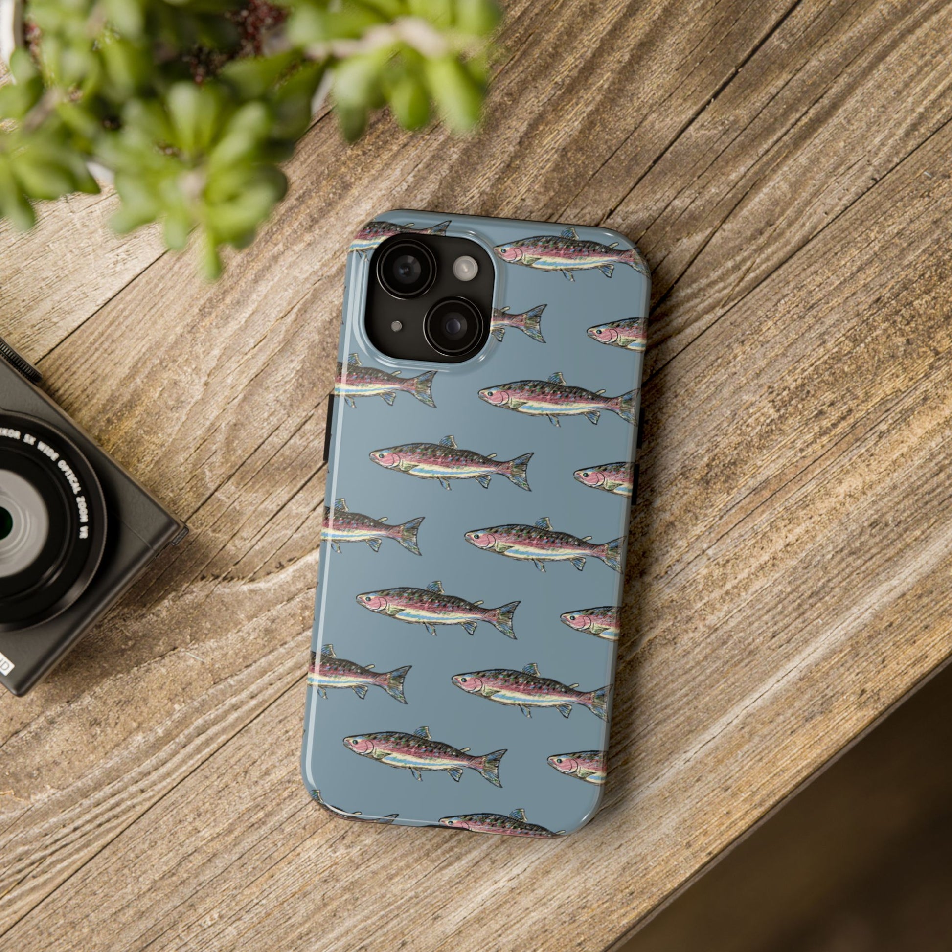 Illustrated rainbow trout durable phone case for anglers on a desk lifestyle view.  Compatible with iPhone and Samsung Models. 