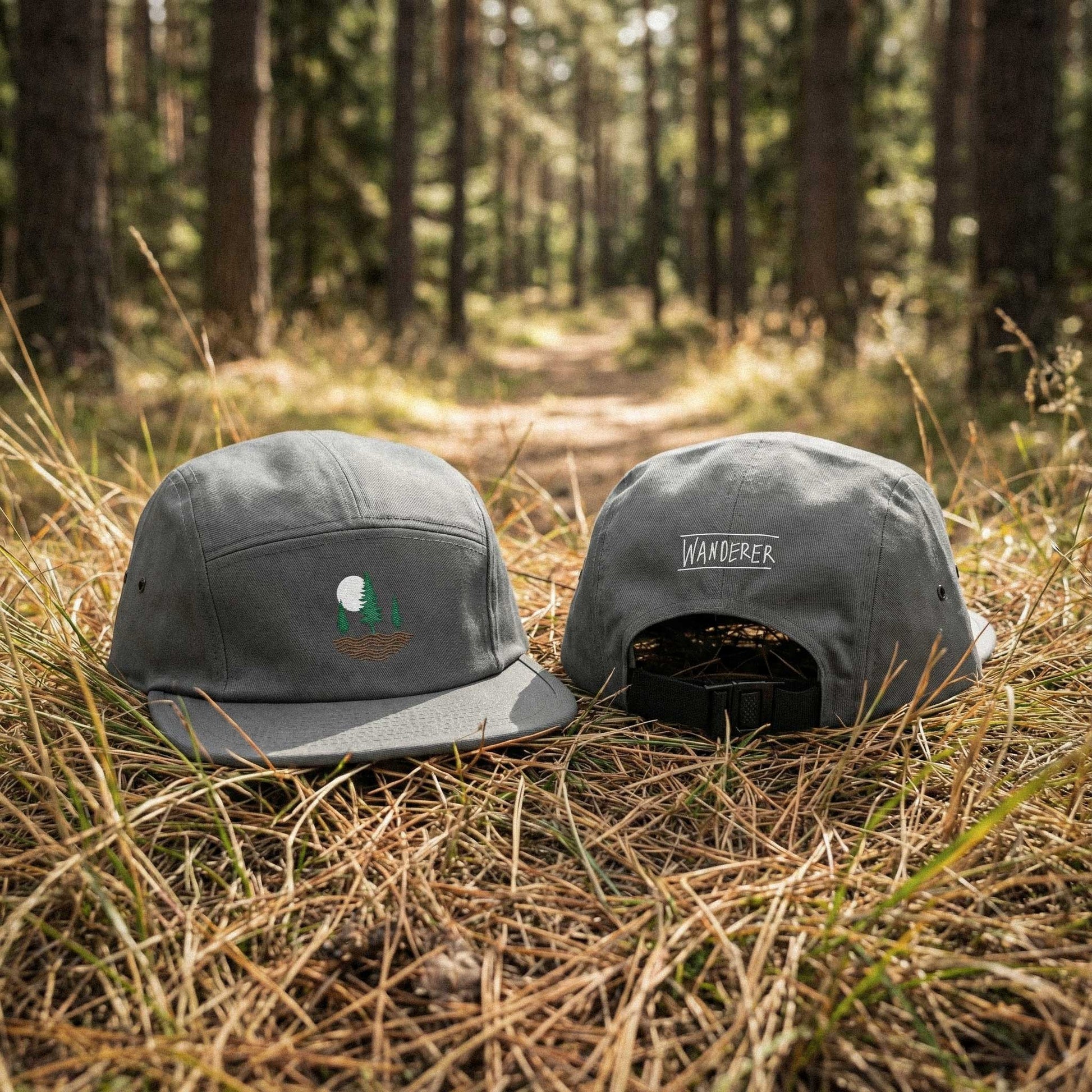Front and back view of grey low-profile cap with embroidered design of three pine trees, a rising sun, and ripple lines symbolizing the earth on a forest floor.