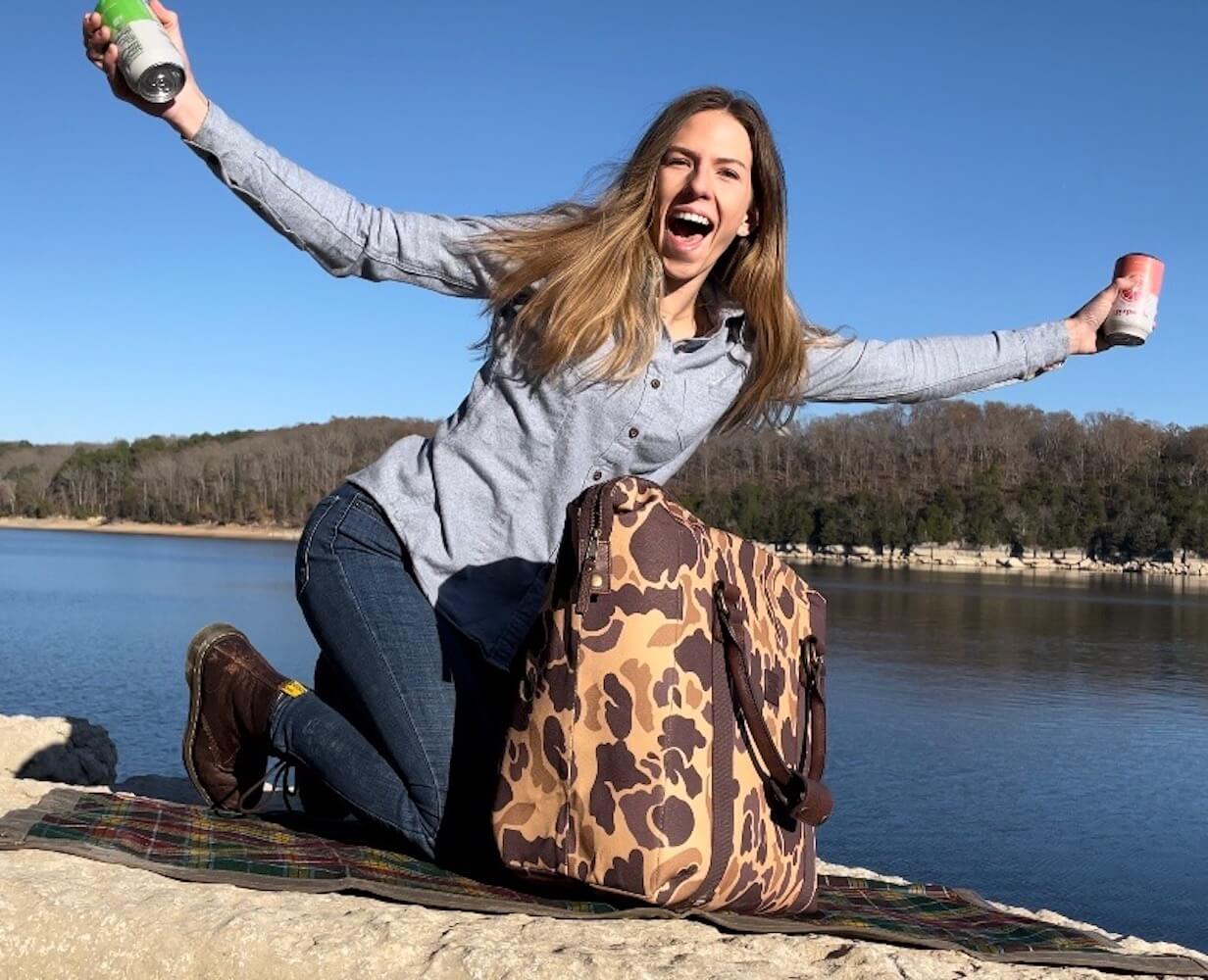Female model near lake using the White Wing Waxed Canvas Large Cooler - 35L in Smoke-Vintage-Camo by Mission Mercantile Leather Goods.