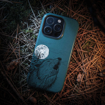 Rugged lifestyle shot of the Wild Wolf Howling phone case on a bed of pine needles in a New England forest setting.